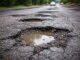 Das Bild zeigt eine stark beschädigte Asphaltstraße mit mehreren großen Schlaglöchern.